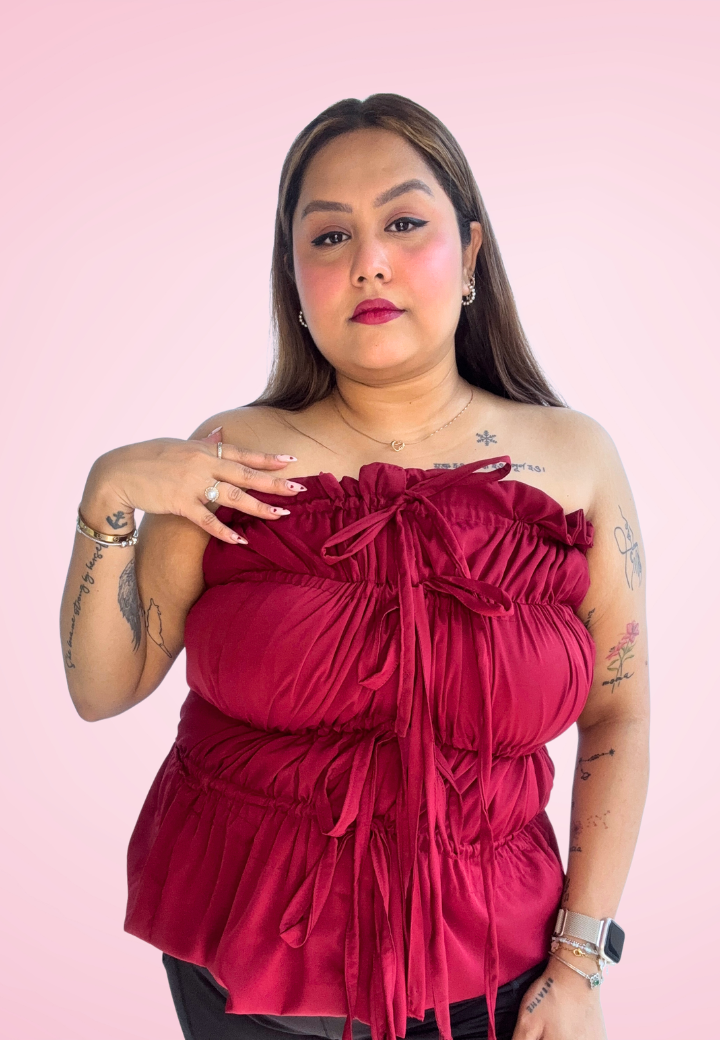 A person wearing a red ruched top against a pink background.