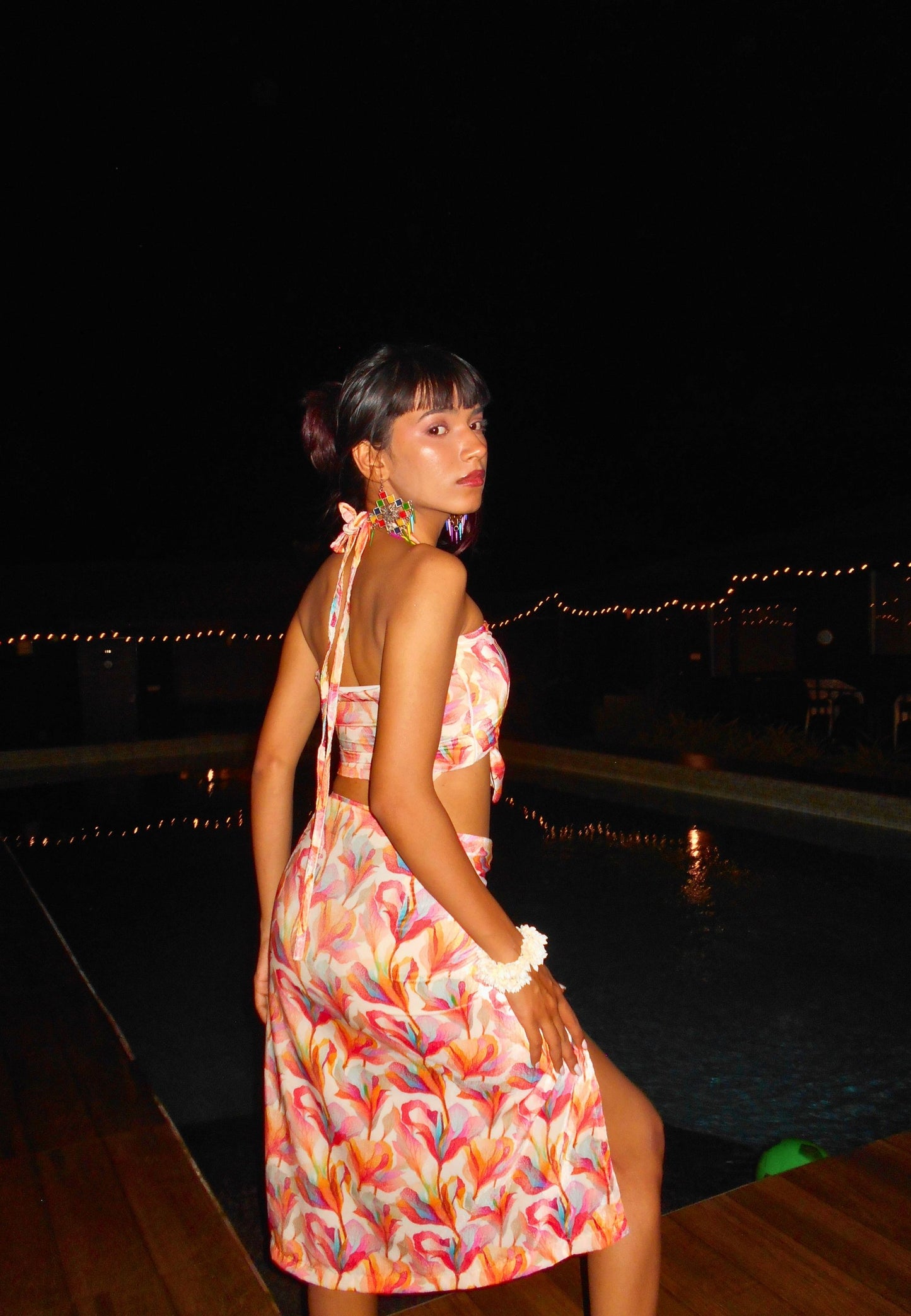 Woman in a colorful dress standing by a pool at night