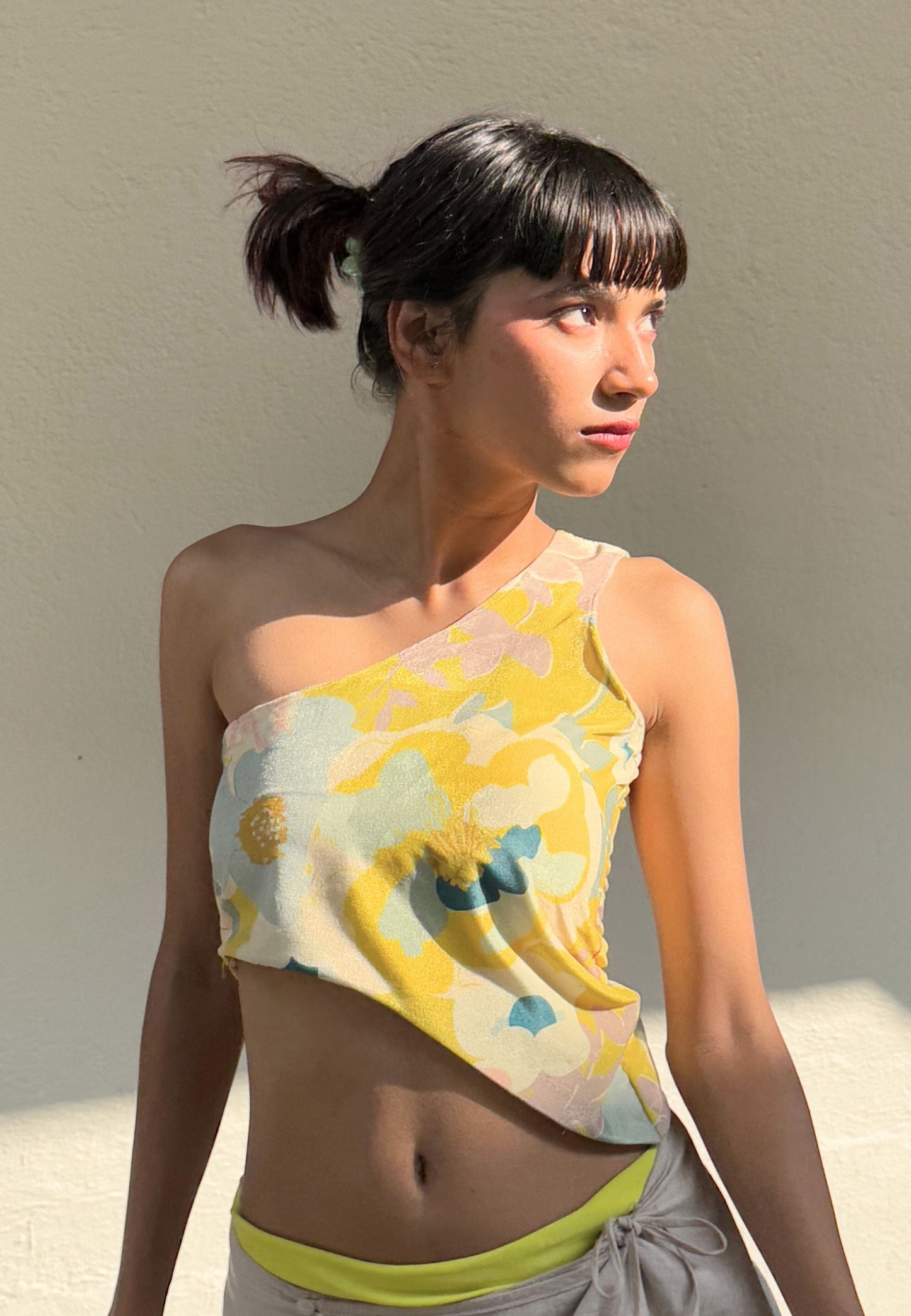 Woman wearing a colorful one-shoulder top against a neutral background