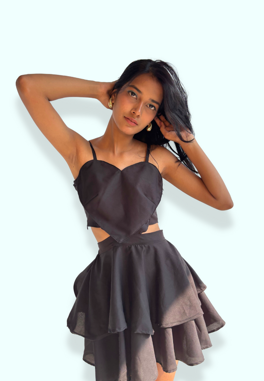 A woman posing in a black dress with a sweetheart neckline and ruffled skirt.