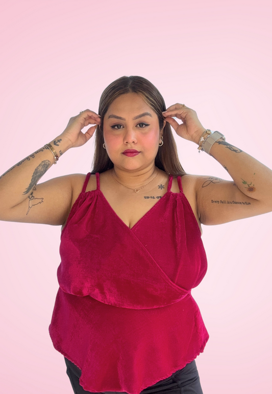 A person wearing a pink peplum top with spaghetti straps and a V-neckline, against a pink background.