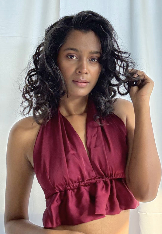 Woman wearing a burgundy halter top against a white curtain background