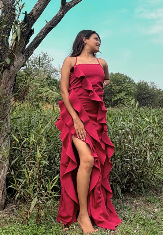 Woman in a red ruffled dress standing outdoors with greenery in the background